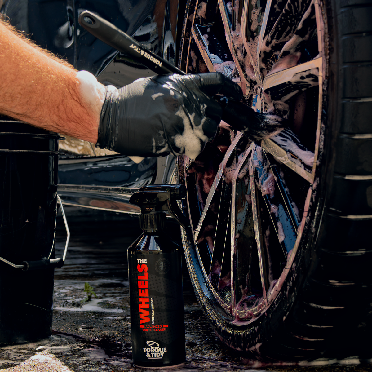Cleaning an alloy wheel with a brush next to The Wheels bottle