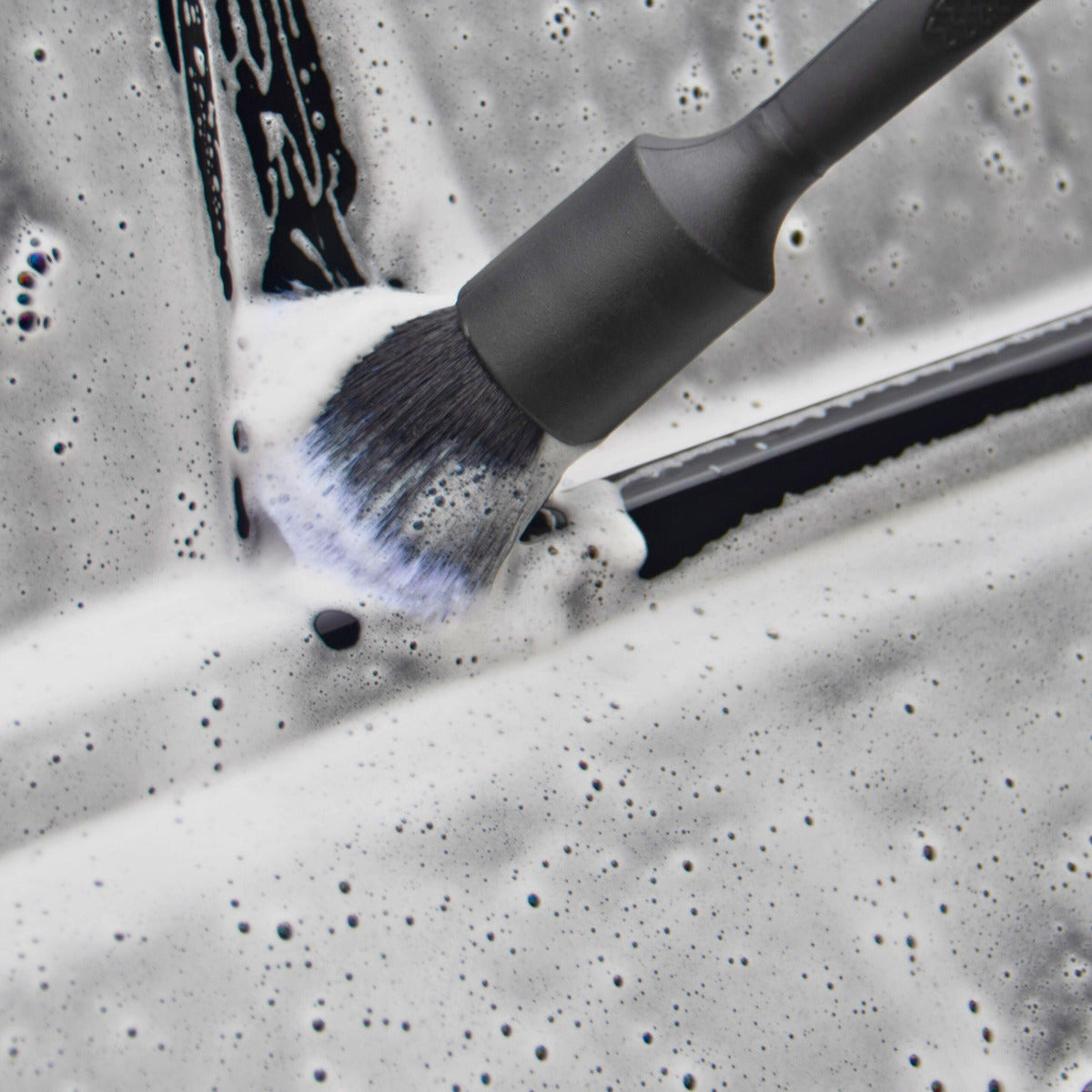 A Torque & Tidy detailing brush cleaning a window trim in snow foam