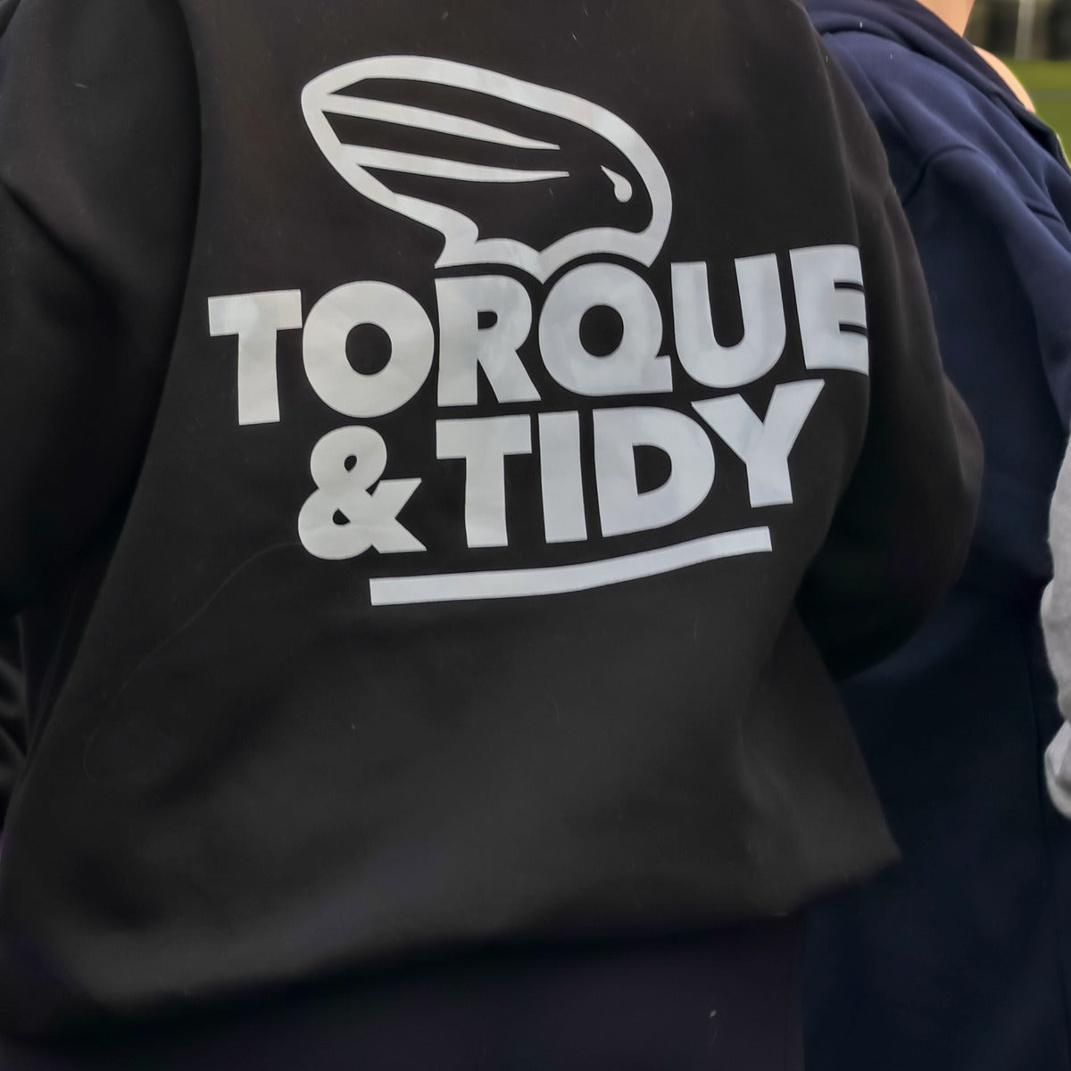 The Torque & Tidy logo on the back of a black T&T hoodie at an event